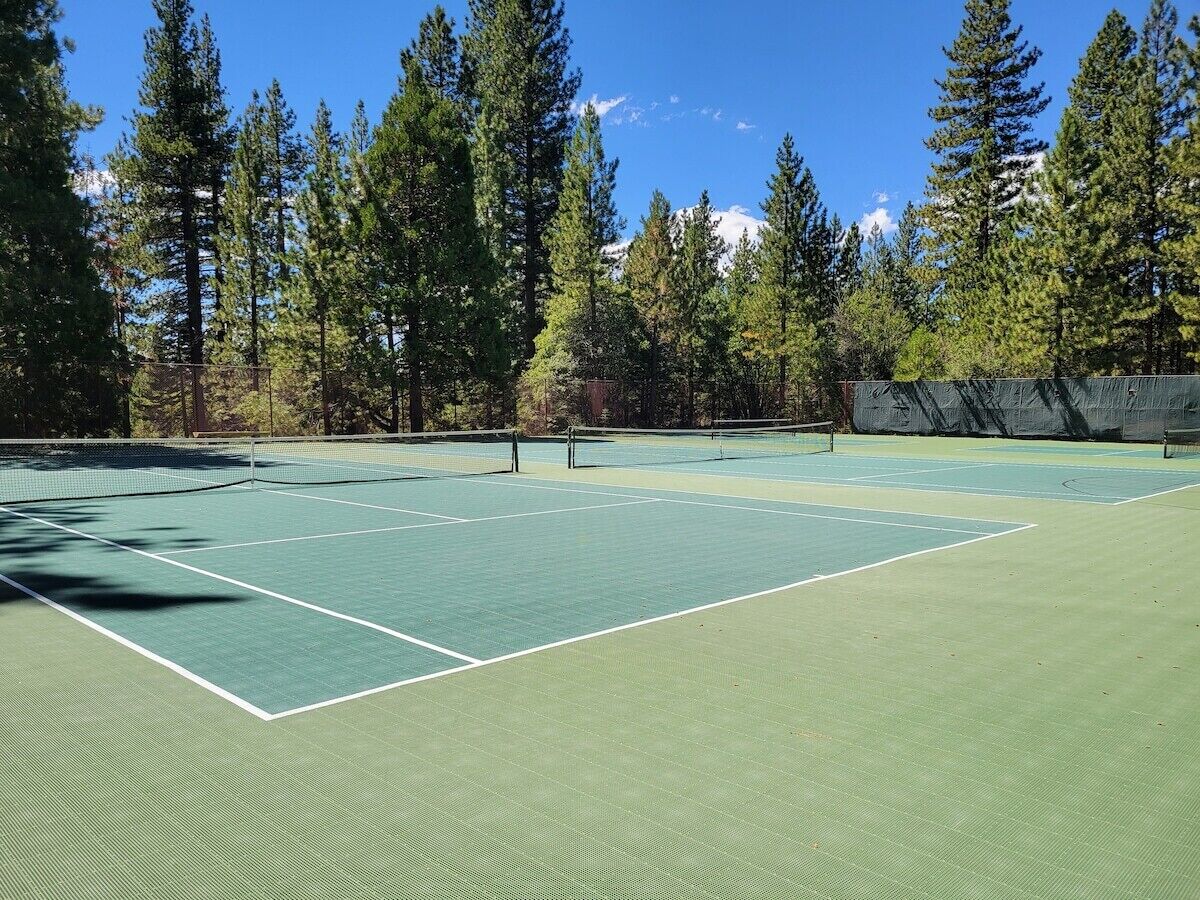 An outdoor tennis court surrounded by tall trees and a clear sky.