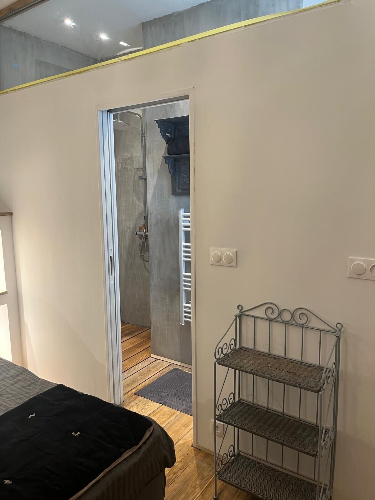 Un dormitorio con cama, un estante metálico y un baño visible a través de una puerta abierta.