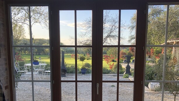 A kitchen with a gas stove and a view of a garden through large windows. - Une Longere de la Puisaye en Fond Dimpasse Avec Parc Apaisant (La Ferté-Loupière)