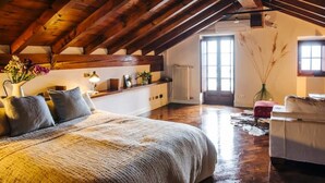 A spacious loft bedroom with a high ceiling, wooden beams, a large bed, a sitting area, and a view of the outside. - Carosa - Luxusberghaus mit Seeblick (Peglio)