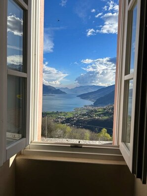Une fenêtre offrant une vue dégagée sur un lac, des montagnes et une ville située en contrebas.