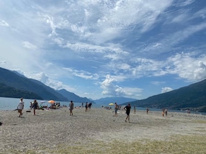 Une plage où l’on voit des gens se promener et se tenir debout, un lac en arrière-plan et des montagnes.