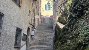 A narrow street with stone steps leading up to a building with a yellow facade and green shutters. - Carosa - Luxusberghaus mit Seeblick (Peglio)
