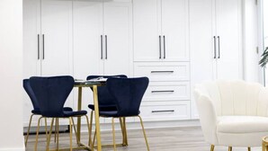 A modern kitchen with white cabinets, two blue chairs, a white chair, and a small round table.