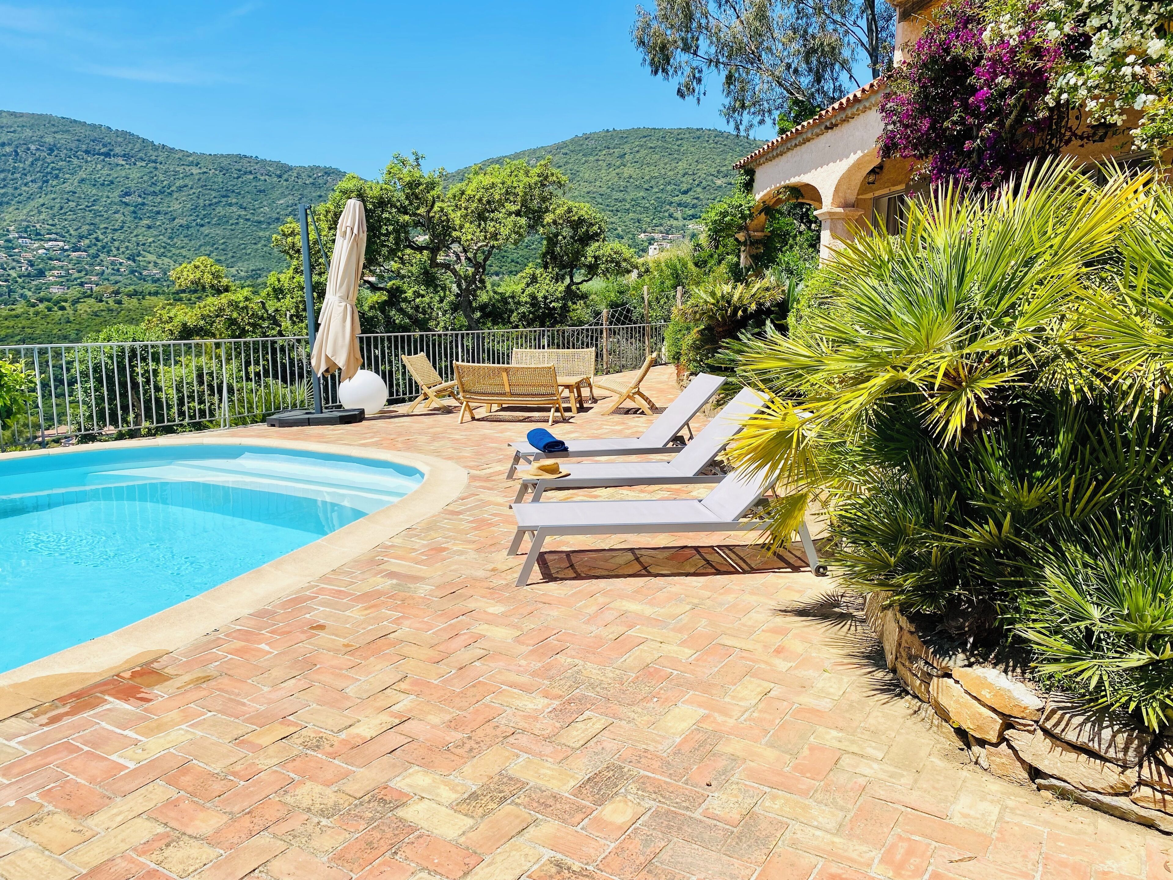A pool area with lounge chairs, a brick patio, and a view of hills.
