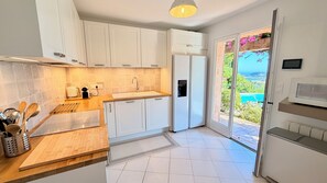 Une cuisine moderne avec des armoires blanches, un four encastré et une vue sur la piscine, accessible par une porte-fenêtre coulissante.