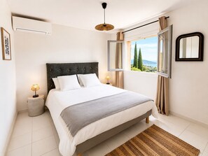 Een slaapkamer met een bed, nachtlampjes, een raam met gordijnen, een spiegel en een airconditioner.