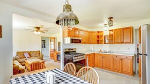 A spacious kitchen with wooden cabinets, a gas stove, and a refrigerator. There is a dining area with a checkered tablecloth and chairs. - Vacation Rental Near South Dakota State University (Aurora)