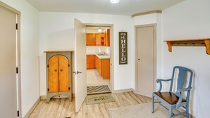 A hallway with a wooden door, a blue chair, a doormat, and a kitchen visible through an open door. - Vacation Rental Near South Dakota State University (Aurora)