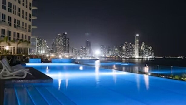 A nighttime view of a swimming pool with city lights in the background. - STUDIO APARTMENT OCEAN VIEW (Panamá)
