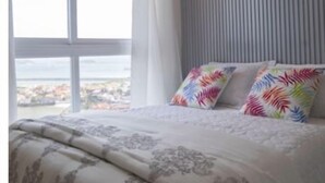 A bedroom with a large window, a bed with patterned bedding, and a view of the sea. - STUDIO APARTMENT OCEAN VIEW (Panamá)