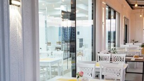 A modern dining area with white furniture and large windows. - Reikartz Abis Tashkent (Tashkent)
