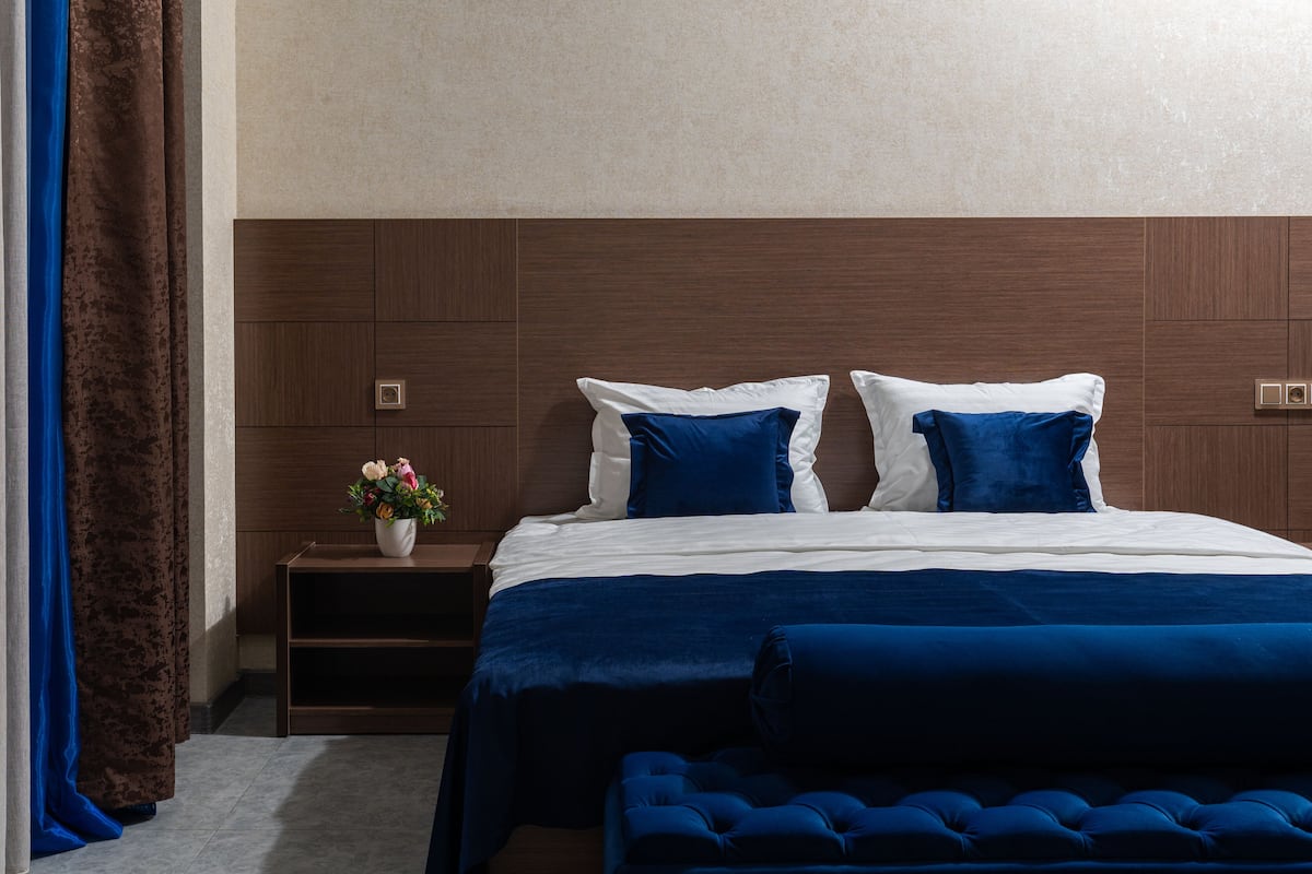A bedroom with a large bed, a nightstand, and a blue upholstered bench.