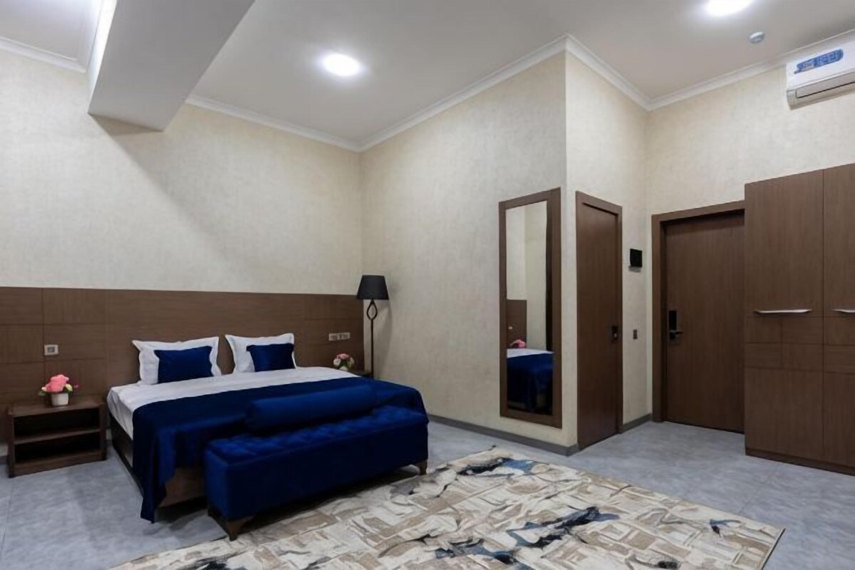 A bedroom with a bed, bedside table, mirror, wardrobe, and a rug.