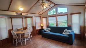A cozy room with a wooden floor, a blue sofa, and a dining table with chairs. There are large windows with blinds, a ceiling fan, and a sign that says "Welcome". - The Lakeview at Northside Marina & Resort (chico)