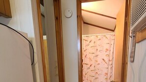 A narrow hallway with wooden flooring leading to a bathroom with a shower curtain featuring fish patterns. - The Lakeview at Northside Marina & Resort (chico)