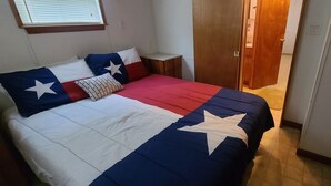 Une chambre à coucher avec un lit orné d’un motif représentant le drapeau du Texas, une table de chevet et une porte en bois.