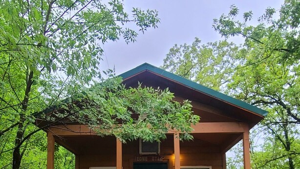 Une cabane en bois avec une porte verte, une véranda avec un banc et un petit escalier menant à l’entrée.