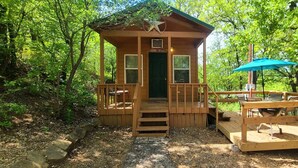 Une petite cabane en bois dotée d’un porche, d’un coin repas avec des sièges extérieurs et d’une décoration en forme d’étoile sur le toit.
