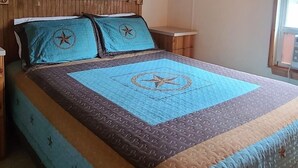 Quarto com teto de madeira, cama com colcha estampada e janela com persianas.