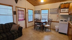 Um espaço de estar compacto com sofá, mesa de jantar, cadeiras e cozinha equipada com fogão, micro-ondas e pia.