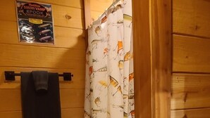 Ein Badezimmer einer Holzhütte mit Duschvorhang mit Fischmuster, einem Handtuchhalter und einem Poster an der Wand.