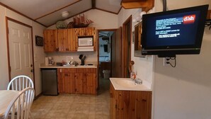 A compact kitchen with wooden cabinets, a microwave, a sink, and a television mounted on the wall. - The Captains Quarters at Northside Marina & Resort (chico)