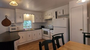 Une cuisine compacte avec des meubles blancs, un four à micro-ondes, une cuisinière et un réfrigérateur. On y trouve un petit îlot central avec un évier et une chaise.