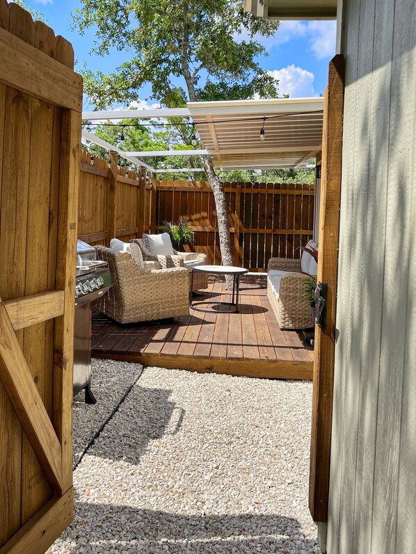 An outdoor patio with a wooden deck, wicker furniture, and a grill.