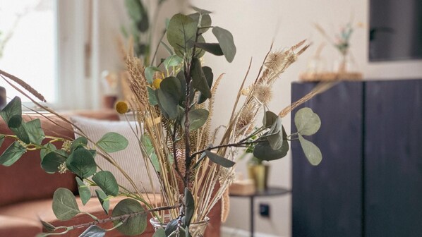 A vase with dried plants and green leaves on a table.