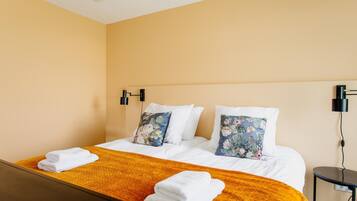 Ein Hotelzimmer mit Doppelbett, zwei Kissen mit Blumenmuster, einer gelben Tagesdecke und zwei Wandlampen.