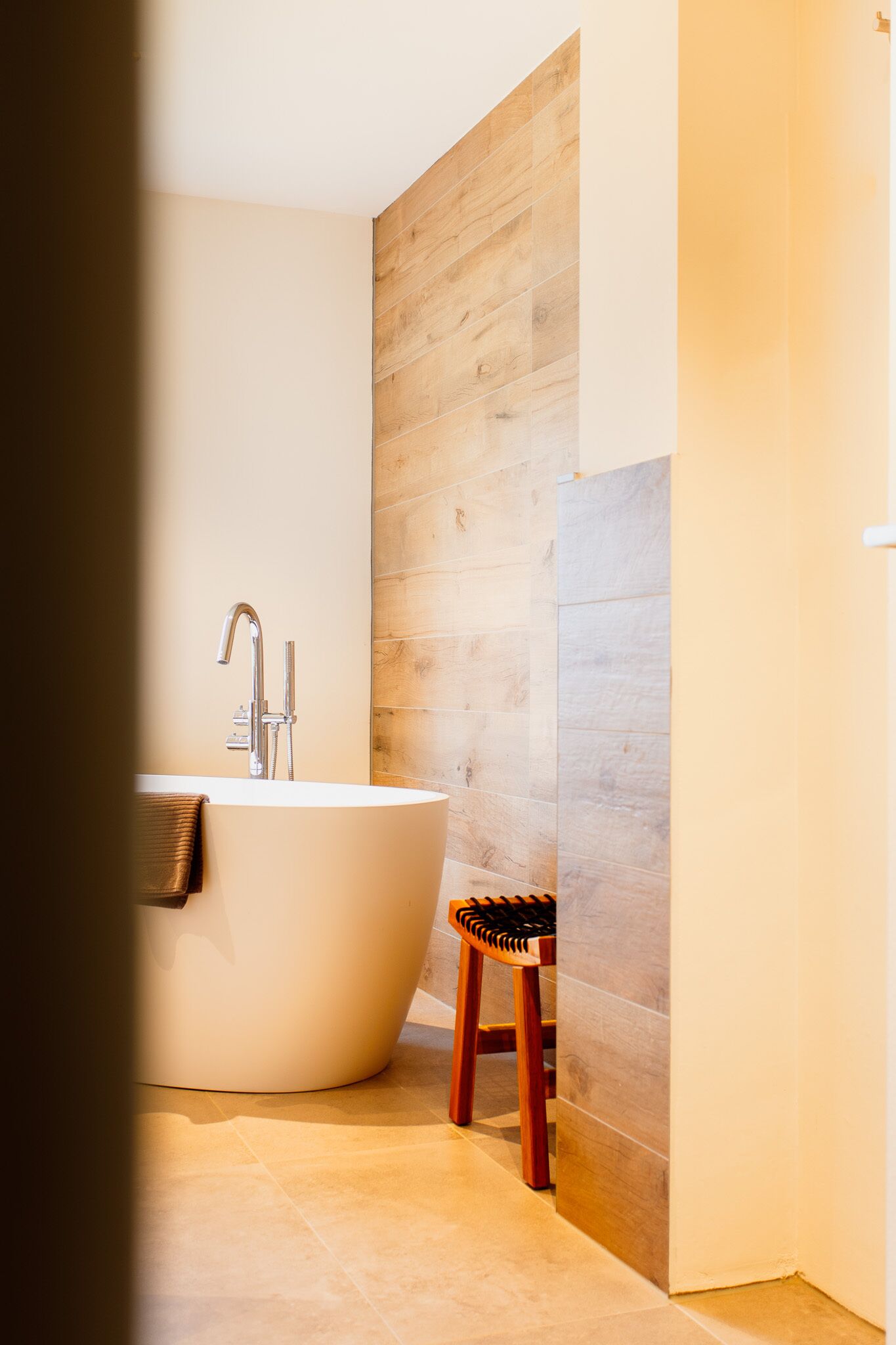 A modern bathroom with a freestanding bathtub, a wooden wall, and a small wooden stool.