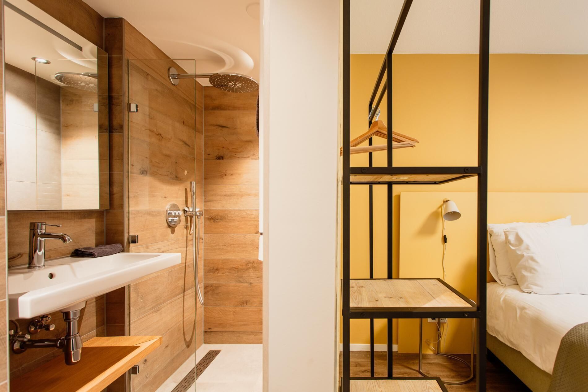 Een moderne badkamer met een houten wastafelmeubel, een douche en een bed met een zwevend plankje.