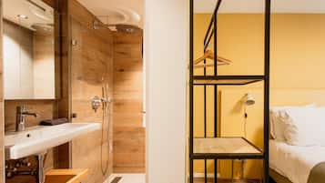 Een moderne badkamer met een houten wastafelmeubel, een douche en een bed met een zwevend plankje.