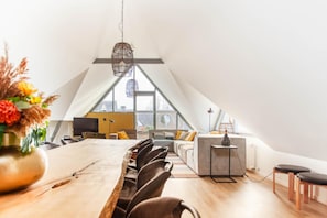 A modern loft bedroom with a large bed, a dining table, and a view of the city through large windows.