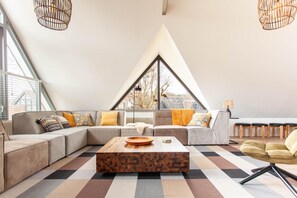 A modern loft with a large window, a sectional sofa, a wooden coffee table, and a checkered floor.