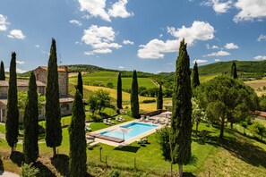 A villa with a swimming pool, surrounded by tall cypress trees and vineyards.