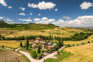 A stone villa with a swimming pool, surrounded by vineyards and rolling hills.