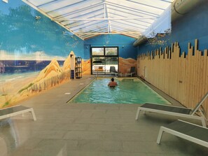 An indoor swimming pool with a desert mural, a wooden fence, and a glass door leading outside.