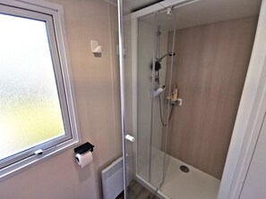 A modern bathroom with a glass-enclosed shower, a toilet paper holder, and a radiator.