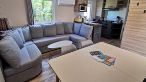 Una sala moderna con un sofá seccional gris, una mesita blanca y una cocina con armarios de madera y un microondas.