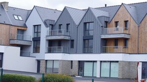 Un edificio moderno de varios pisos con una combinación de paneles exteriores de madera y color gris, ventanas amplias y balcones.
