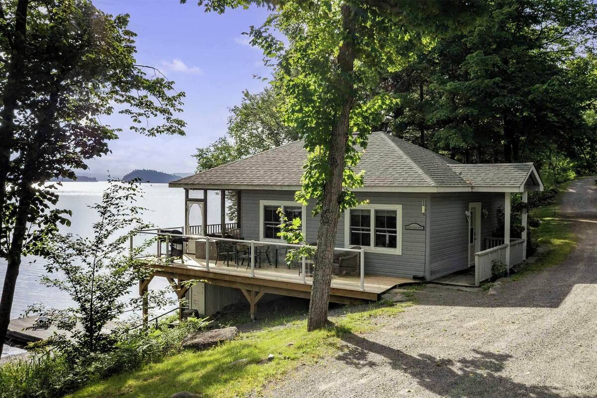 A cabin with a deck overlooking a lake, surrounded by trees.