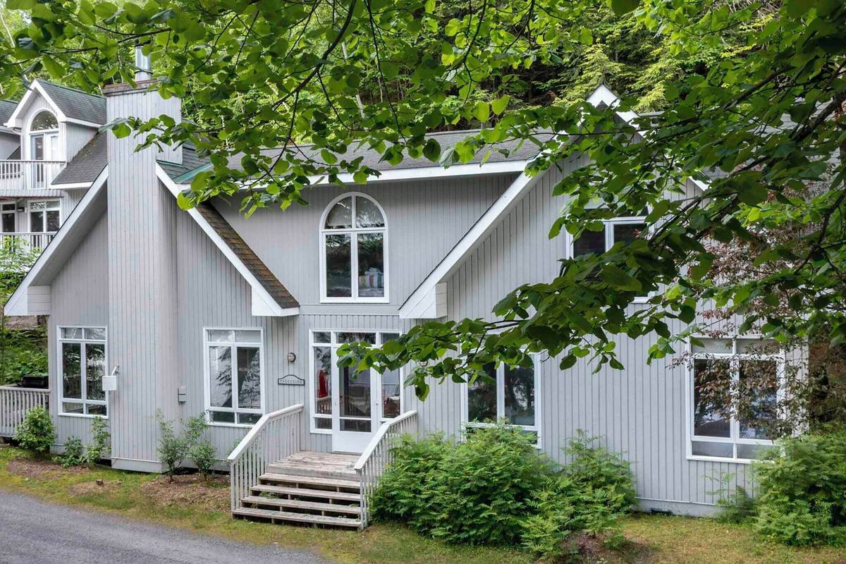 A two-story house with a steeply pitched roof, multiple windows, and a front porch with steps.