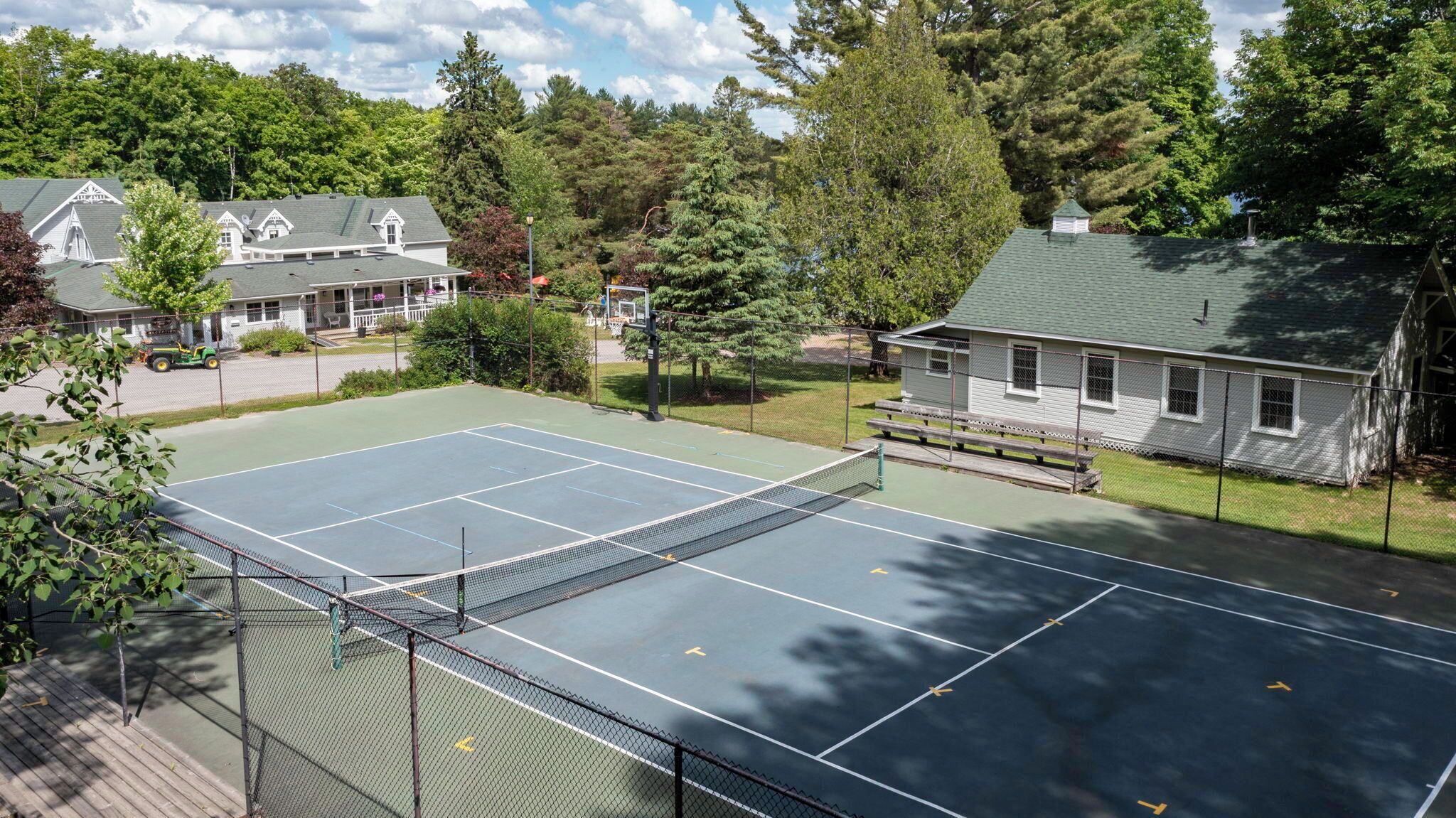 Een tennisbaan met een net, omringd door een hek, naast een gebouw met een veranda.