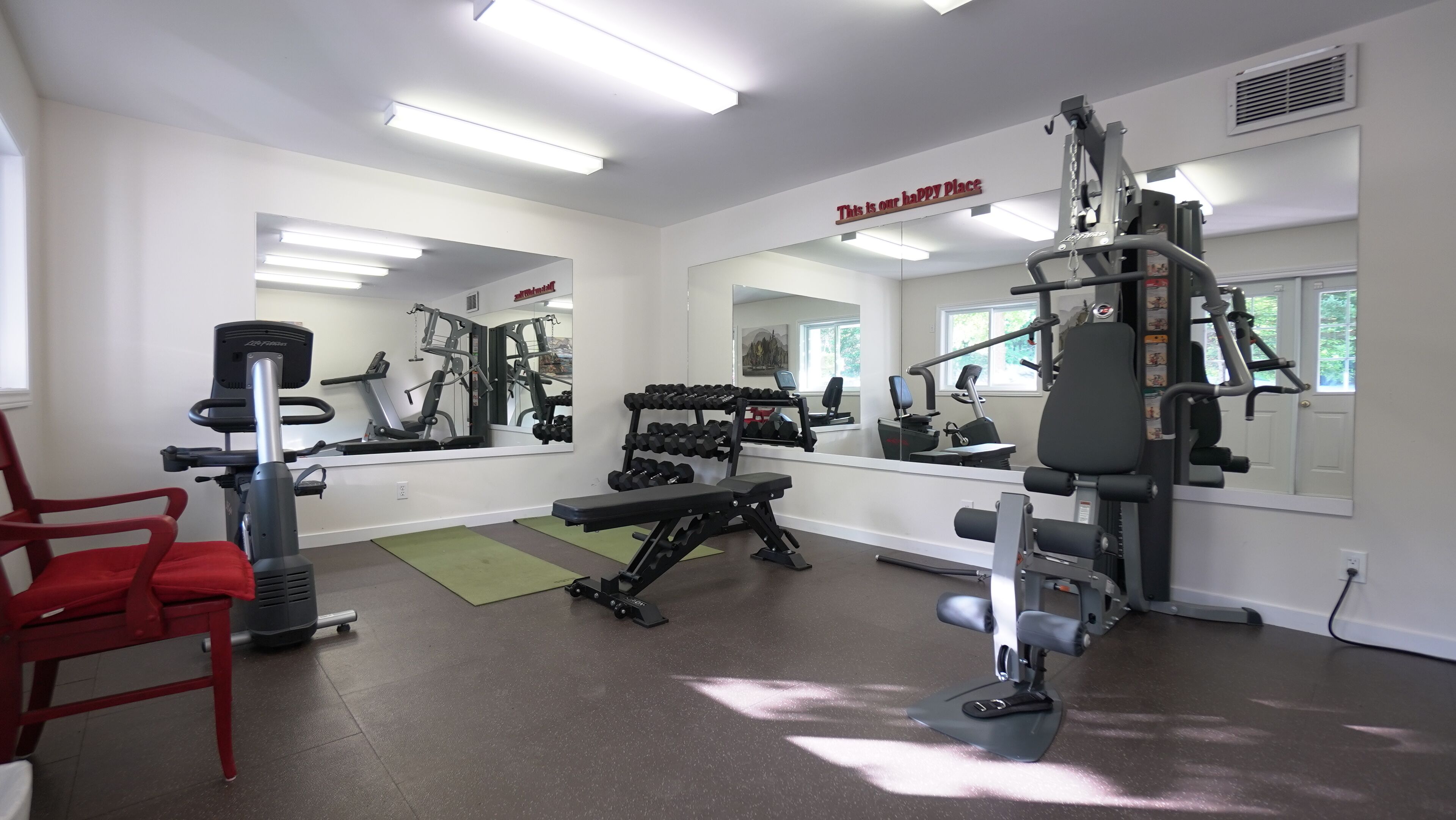 A gym with exercise equipment, a red chair, and a sign that says "This is our happy place".