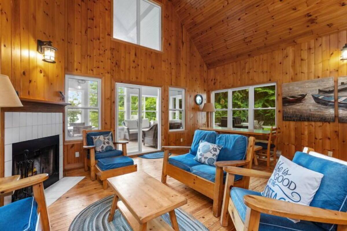A cozy cabin interior with wooden walls, a fireplace, a sofa set, and a dining table.