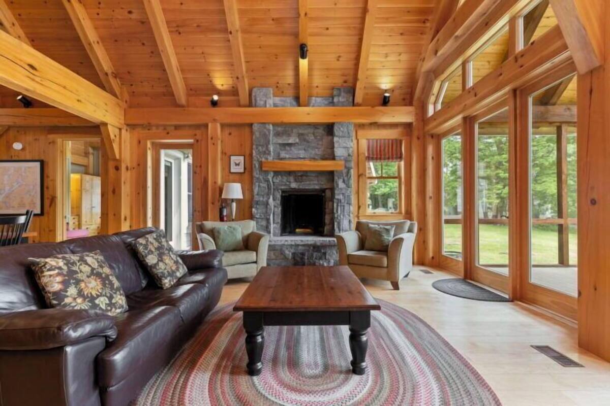 A cozy log cabin interior with a stone fireplace, leather sofa, and large windows.
