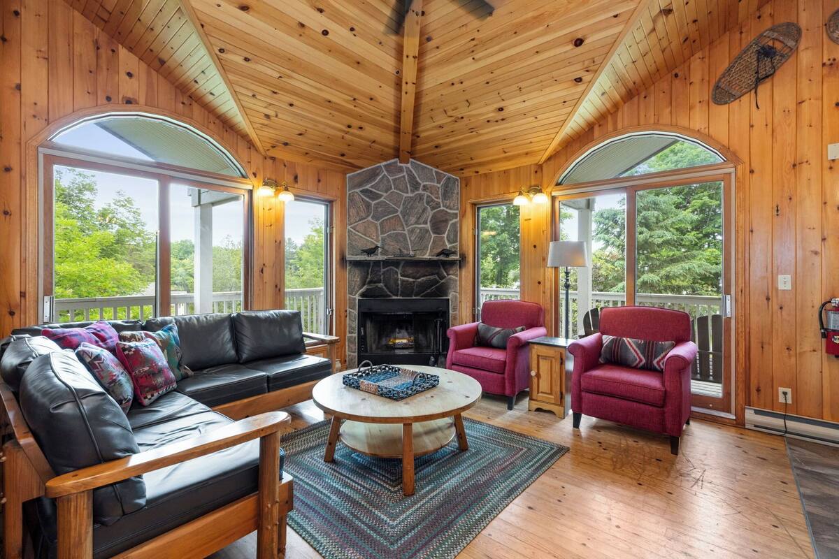 A cozy cabin interior with a stone fireplace, leather sofa, and red armchairs.