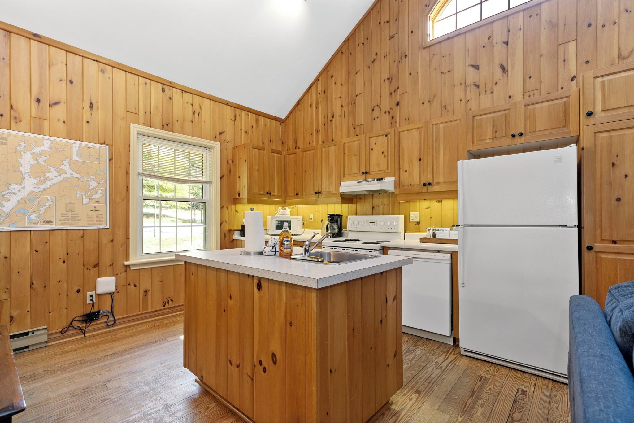 A kitchen with wooden paneling, a central island, white appliances, and a map on the wall.